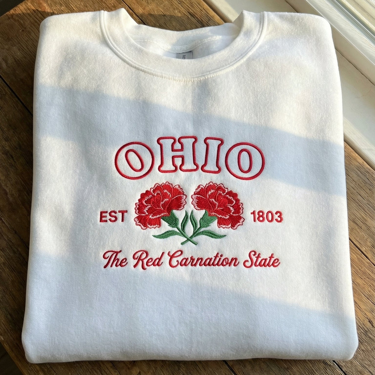 White folded sweatshirt with detailed red Carnation flower embroidery reading Ohio EST 1803 The Red Carnation State