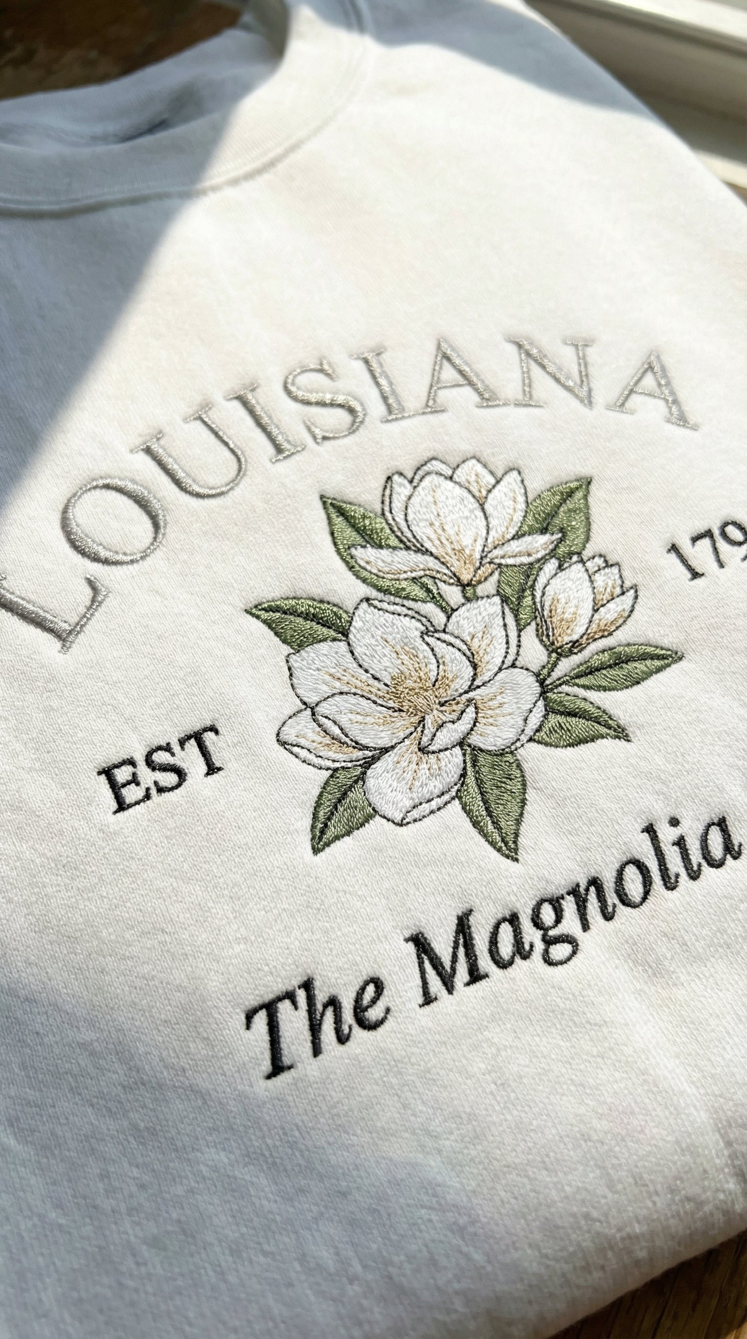 White sweatshirt with embroidered design of magnolias and text on a light background