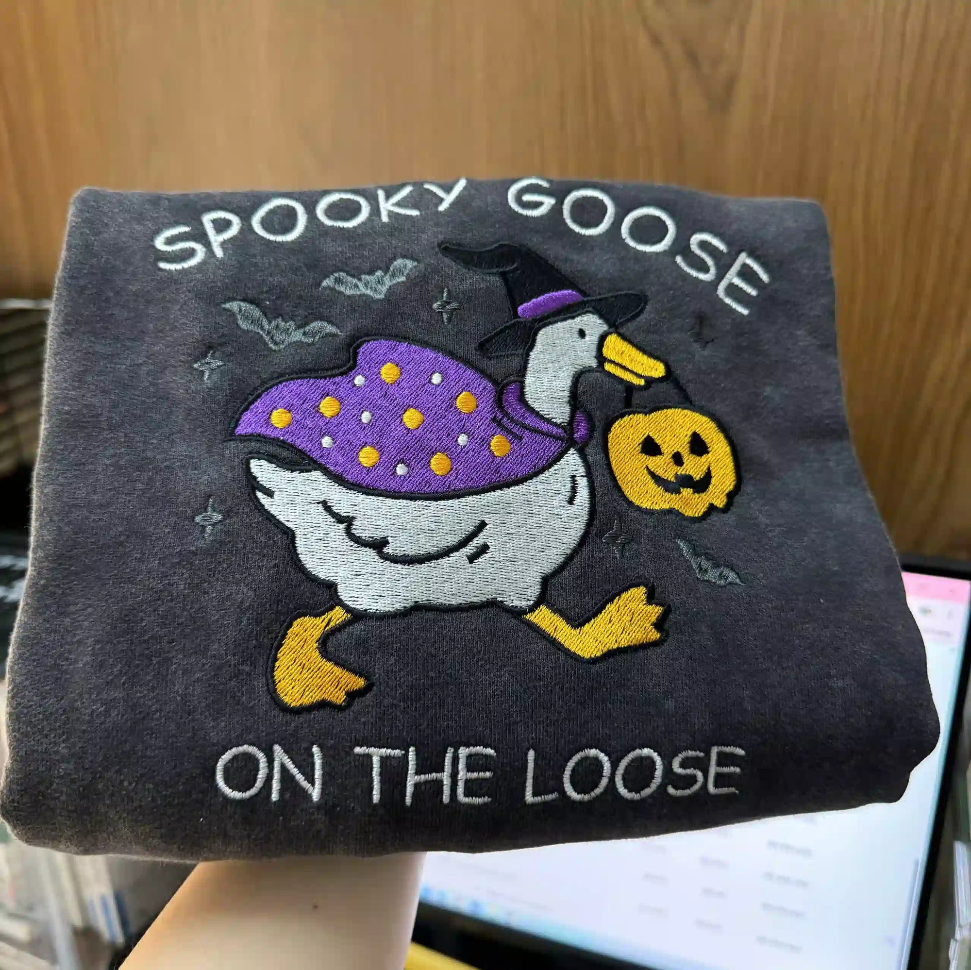 Dark gray shirt with Halloween-themed goose design and text on a wooden surface.