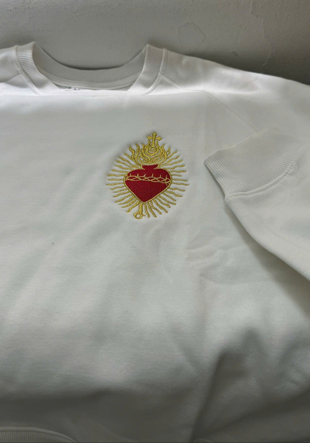 White sweatshirt with a red heart and gold crown design on a plain background