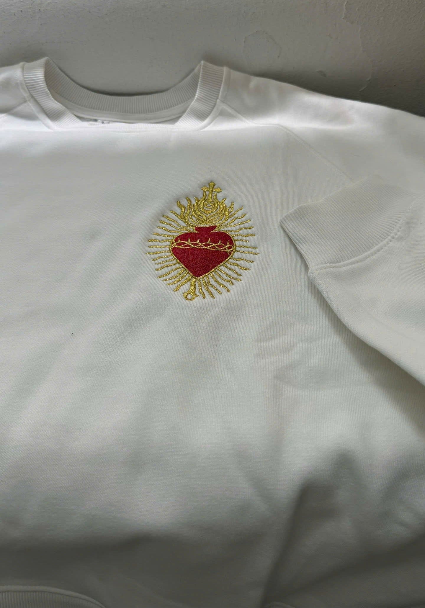 White sweatshirt with a red heart and gold crown design on a plain background