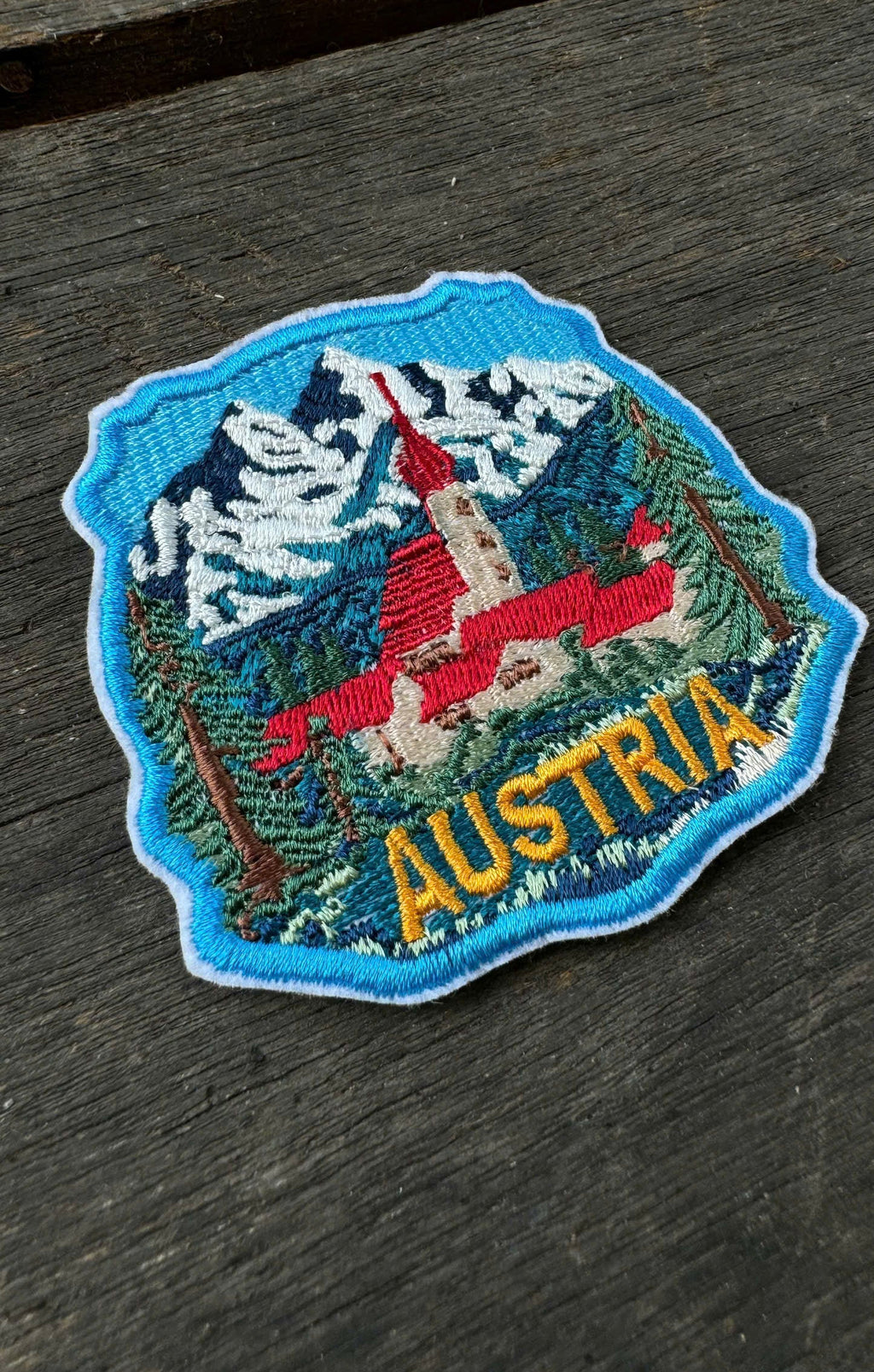 Embroidered patch of Austria with a mountain and traditional red gondola on a wooden surface