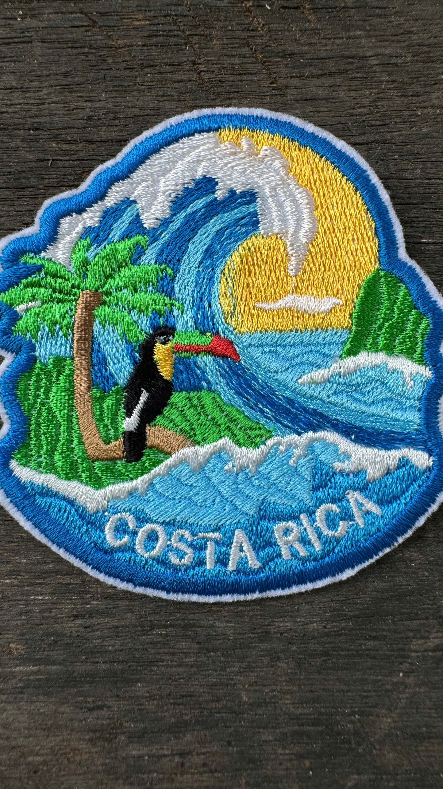 Embroidered patch of Costa Rica with a toucan, palm tree, and wave on a dark surface