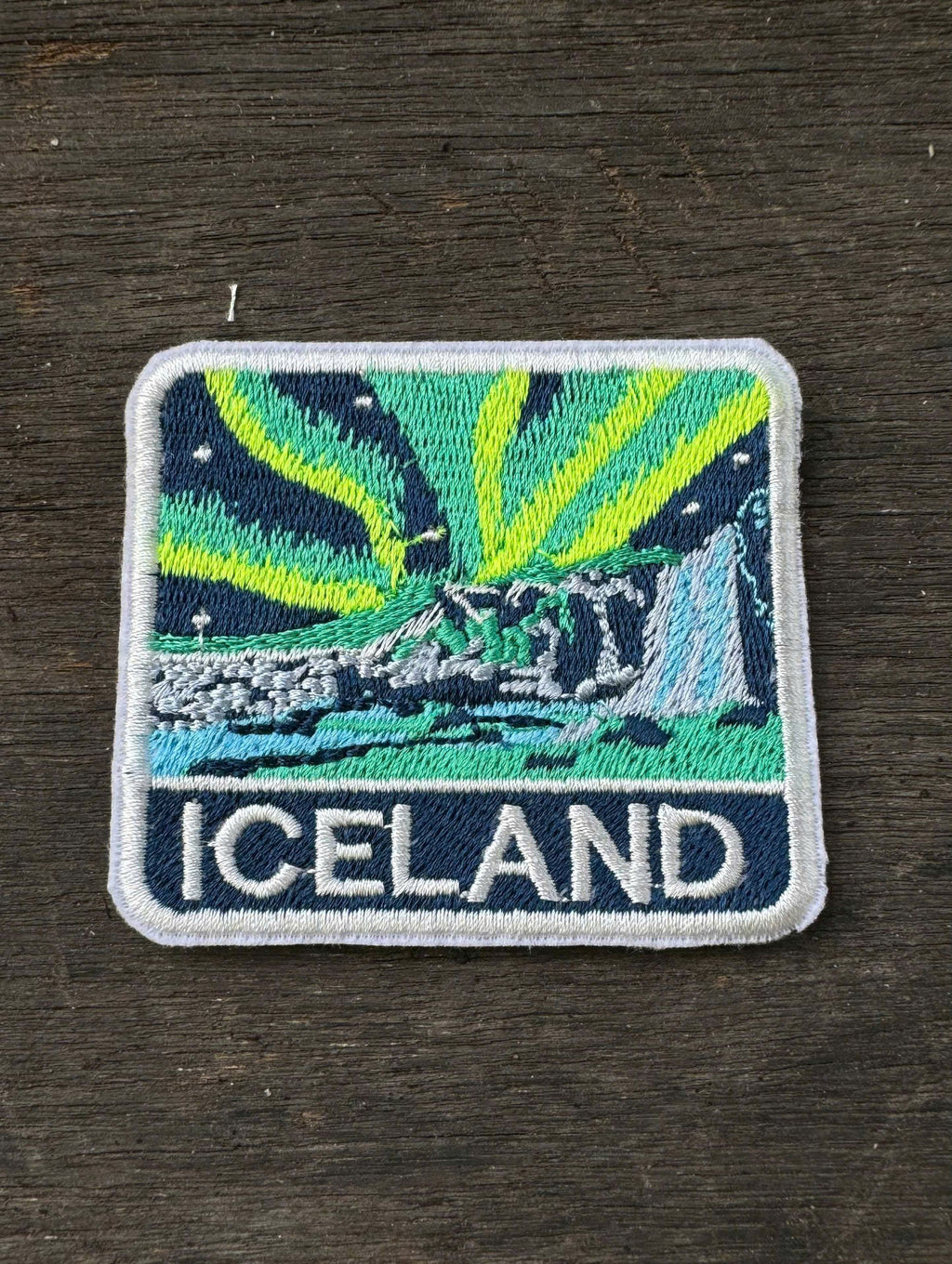 Embroidered patch of Iceland with Northern Lights design on a dark fabric background