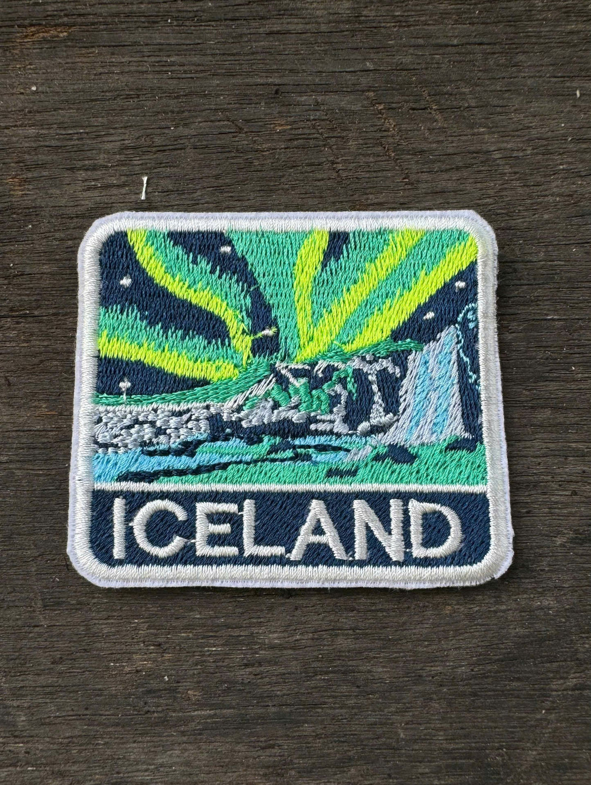 Embroidered patch of Iceland with Northern Lights design on a dark fabric background