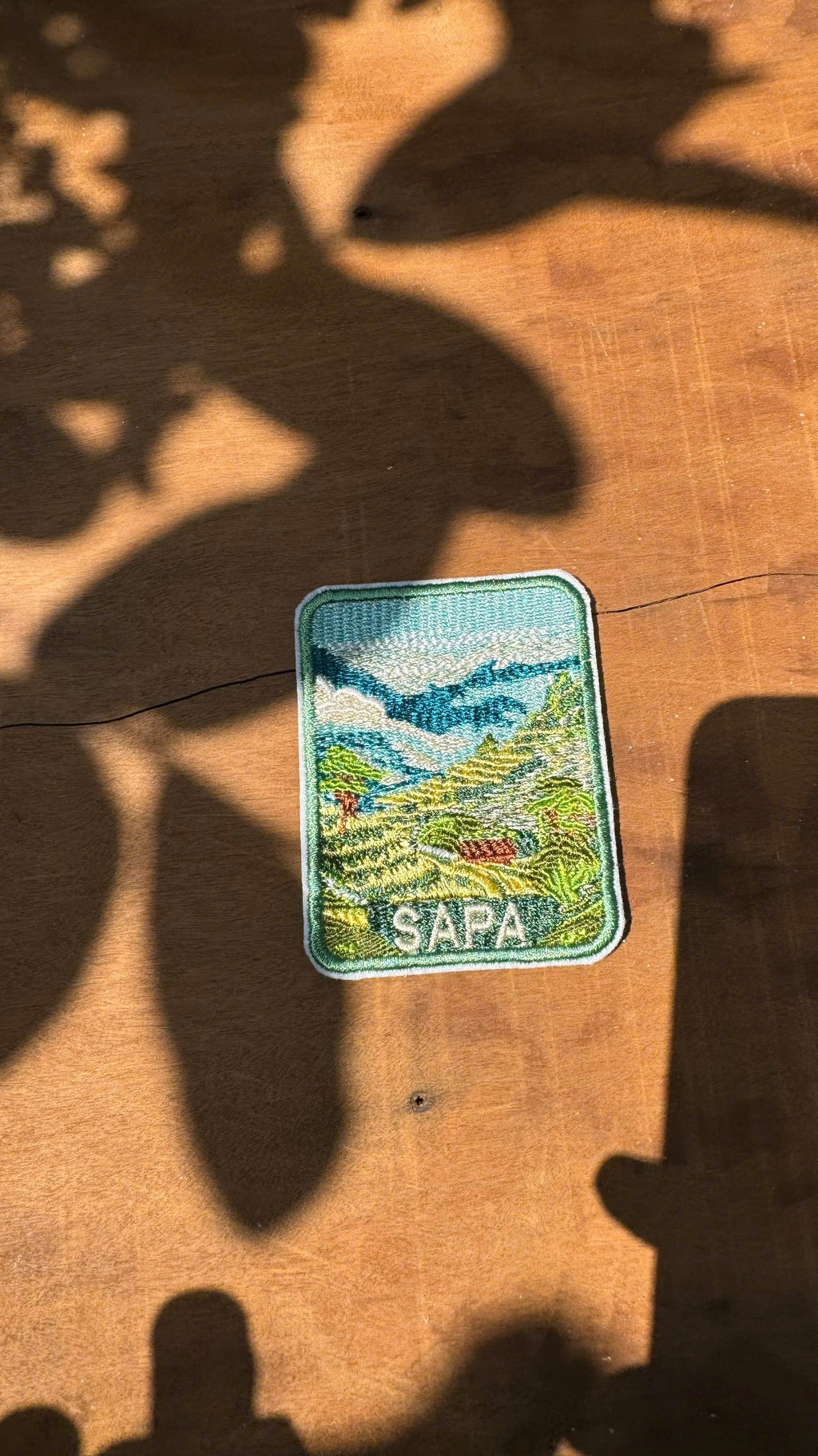 Embroidered patch with a scenic design and 'Sapa' text on a wooden surface.
