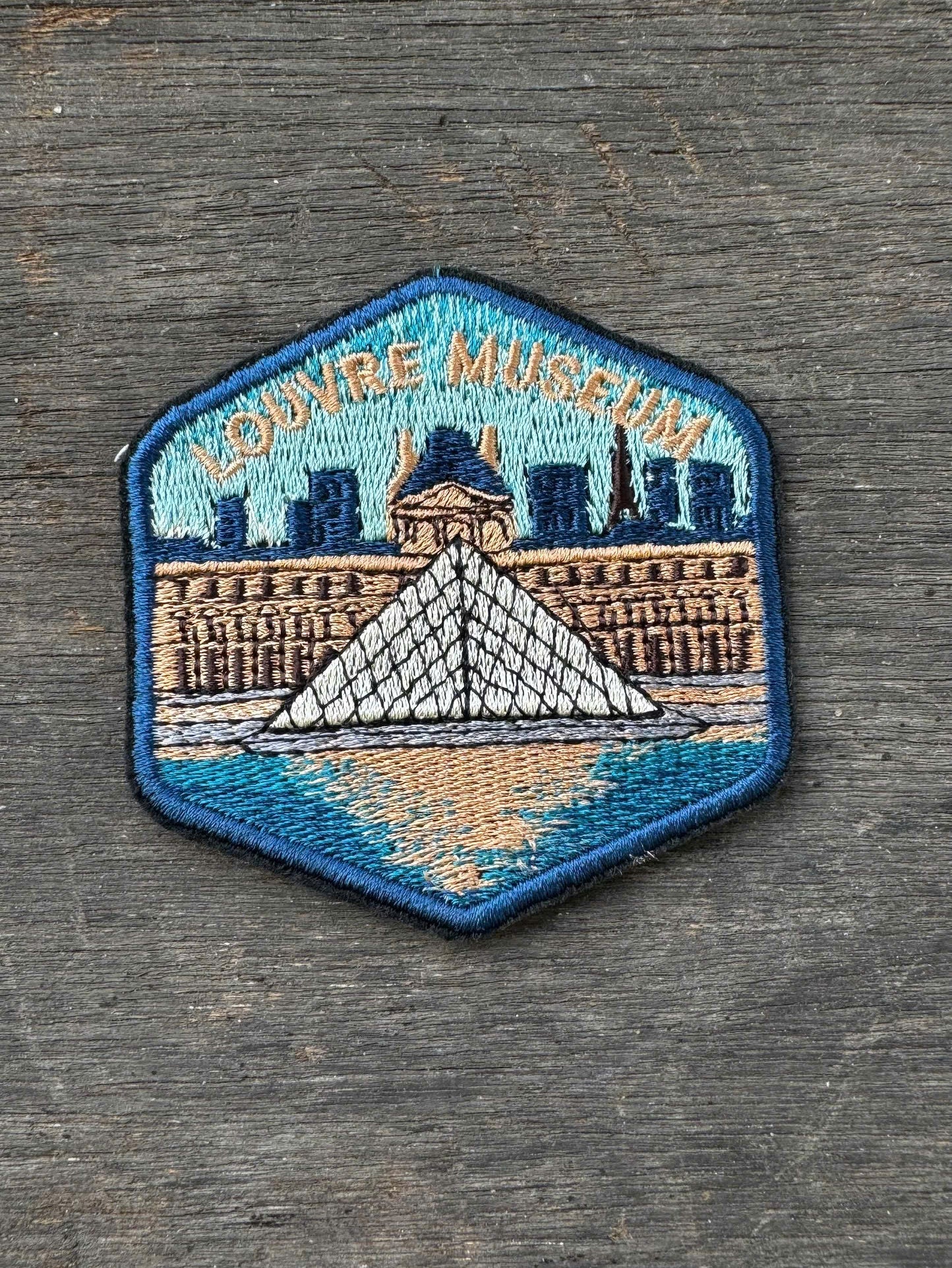 Embroidered patch of the Louvre Museum on a wooden surface
