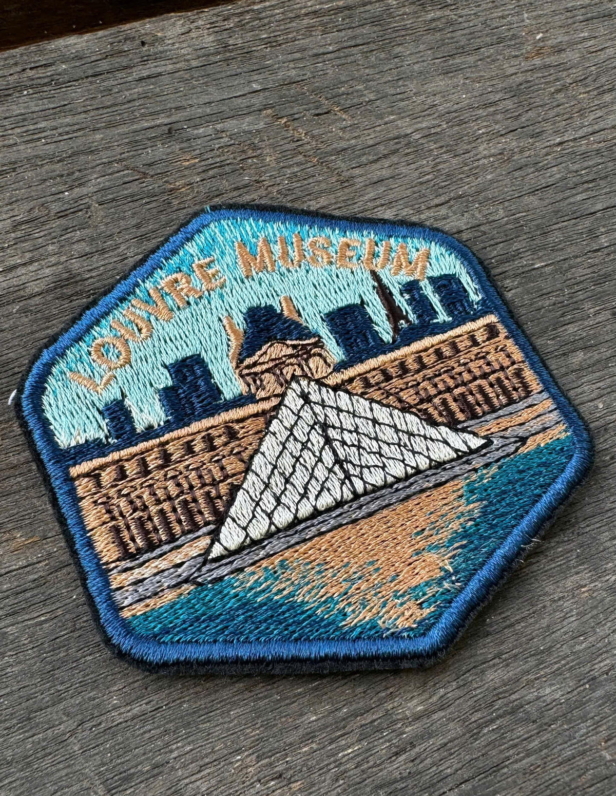 Embroidered patch of the Louvre Museum on a wooden surface